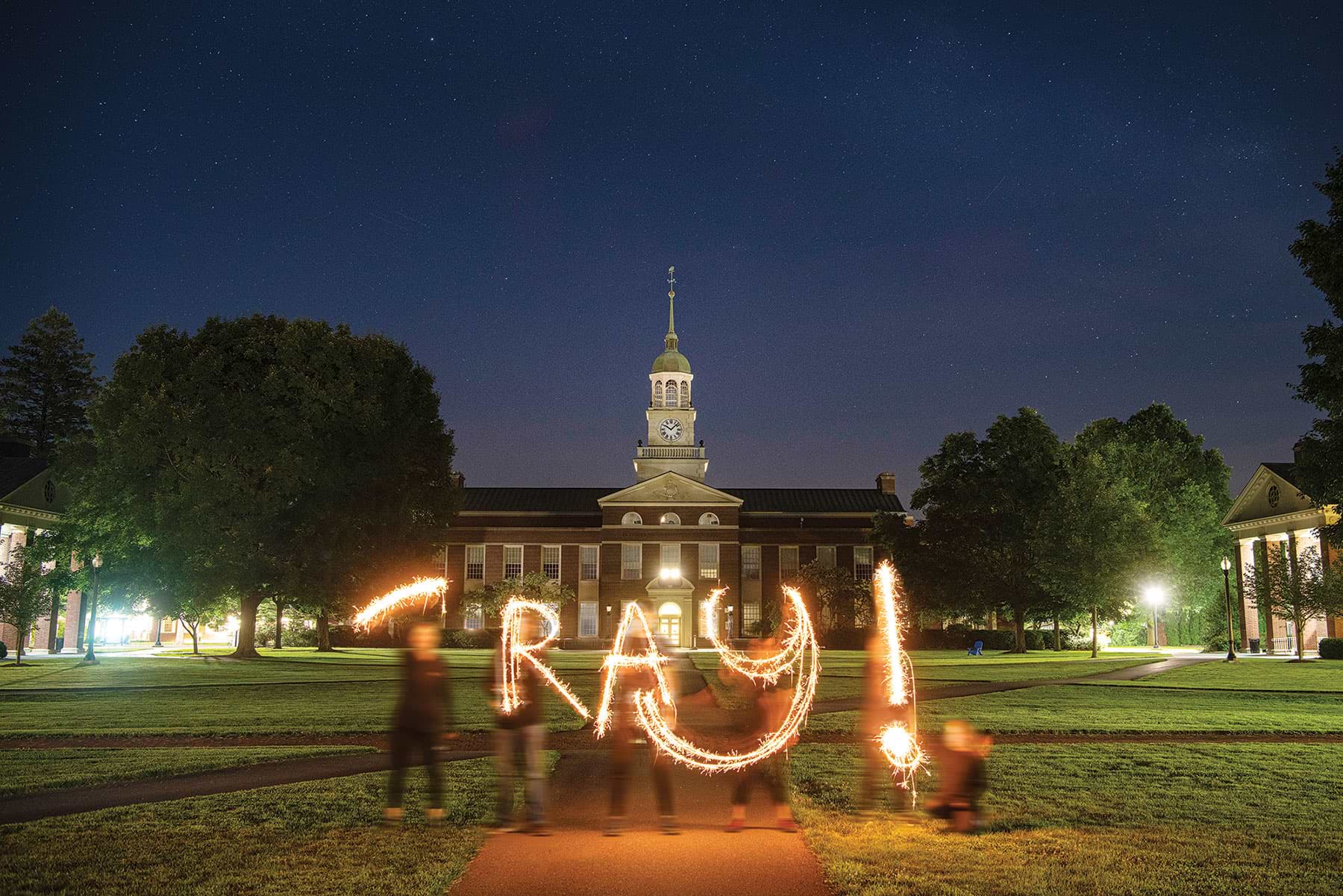 Students writing 'ray with light at night on campus