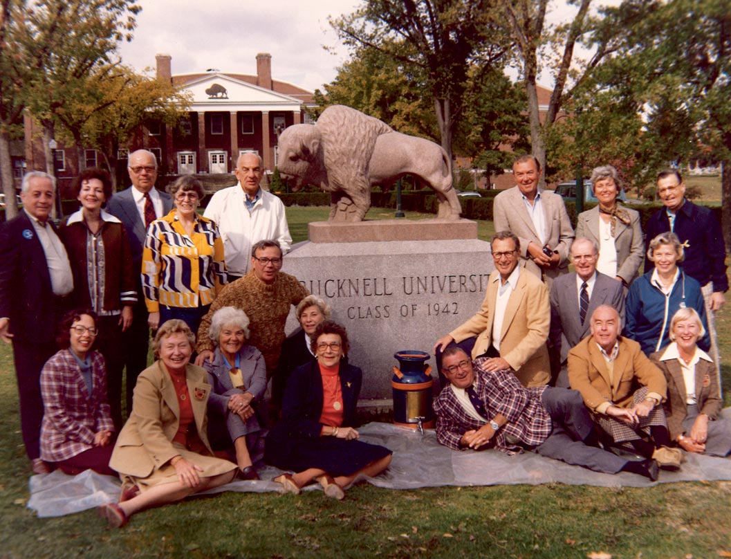 A group picture with members from the class of 1942 in front of the stone class of '42 statue