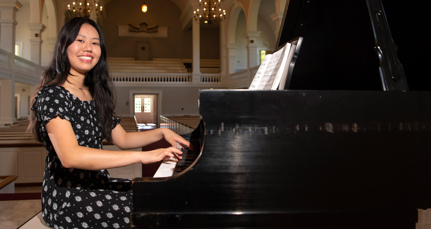 Vivian Kuang smiles sitting at a piano with her hands on the keys