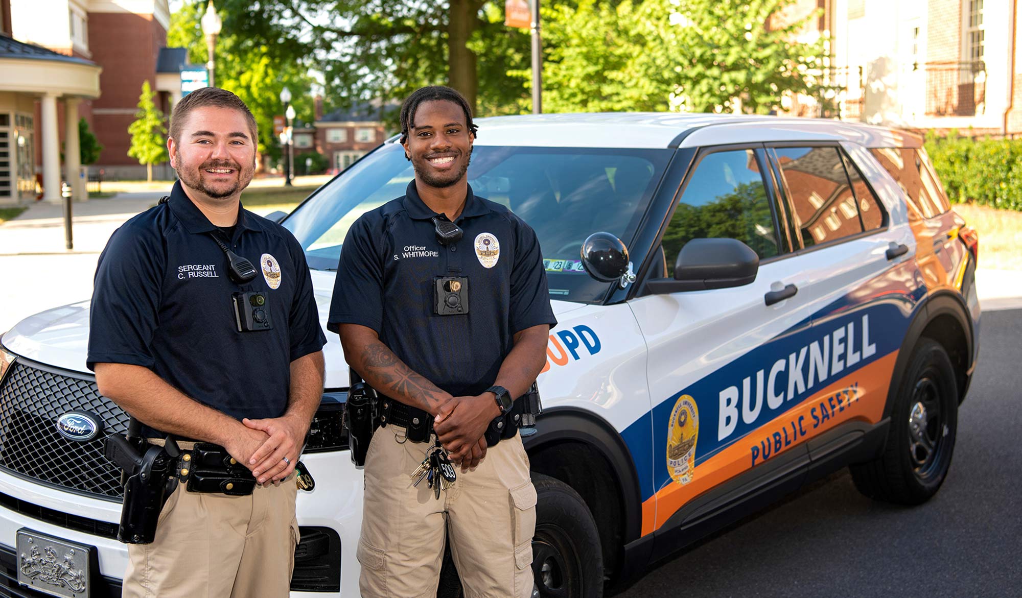 Two Bucknell Pubic Safety Officers posing in front of a Public Safety car