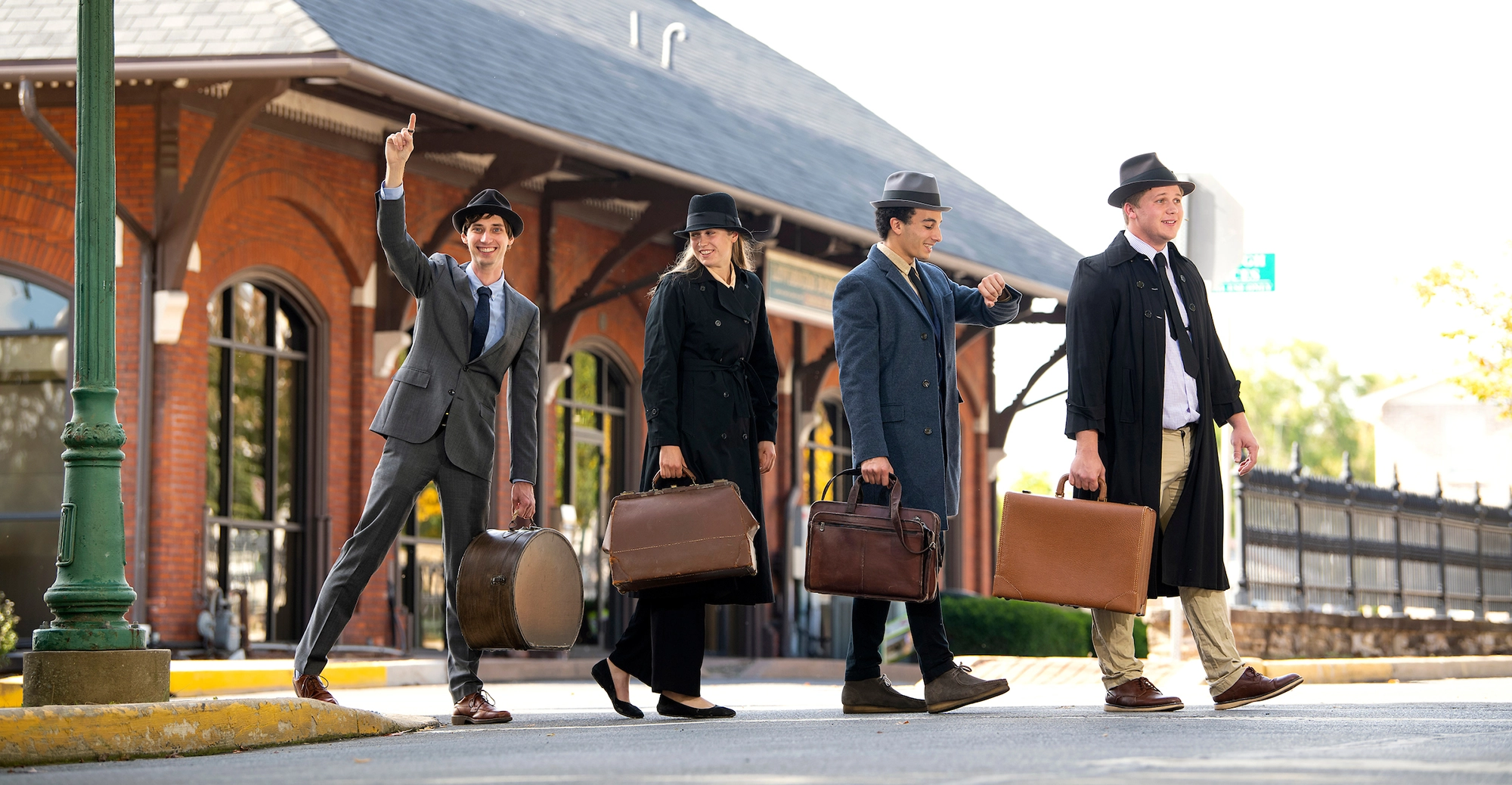 Four individuals are seen carrying suitcases in their respective business attire at a railroad stop/train station posing in a front facing walking path (From left: Professor Sam Gutekunst, Asta Rustad ’23, Yacine Bouabida ’24 and Austin Beal ’24)