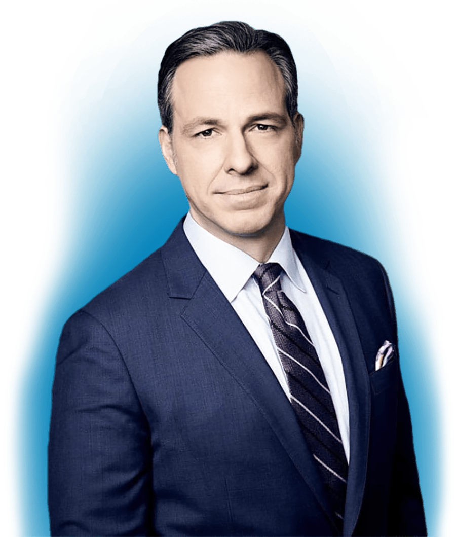 A portrait headshot of Jake Tapper grinning in a navy blue suit and line patterned tie with a vibrant blue gradient glow digital effect placed behind him