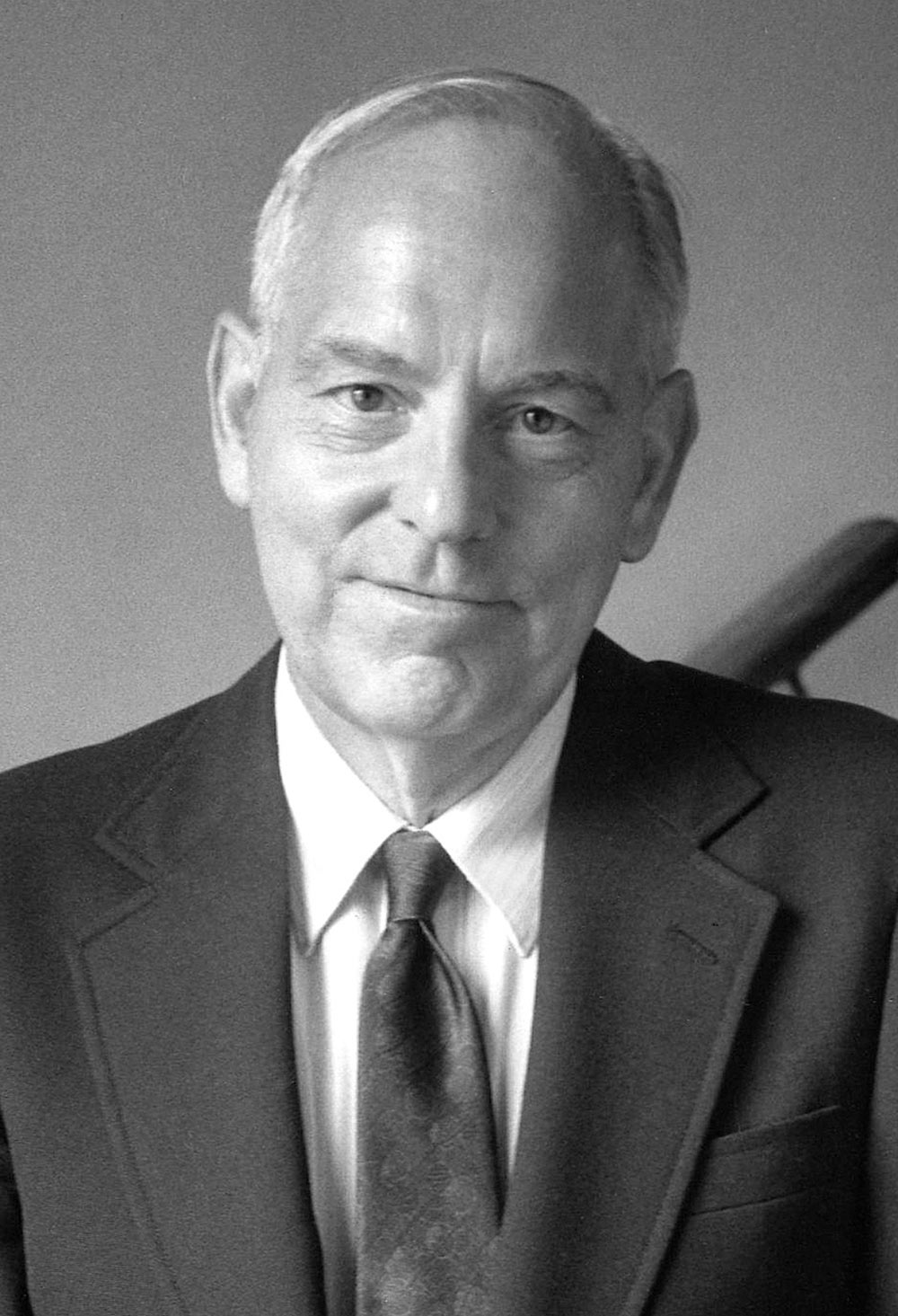 A black and white portrait headshot photograph of Rev. James Hammerlee (Former Bucknell chaplain, steadfast student supporter and lover of the arts) grins in a business suit and tie attire style