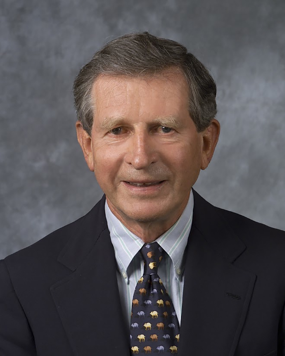 Portrait headshot photograph of Jim Schubauer '56, P'81, G'12, G'15 (Former trustee emeritus for Bucknell University) grinning in a dark navy blue suit and dark grey button-up dress shirt underneath with a multi-colored pattern style on top of a dark navy blue tie