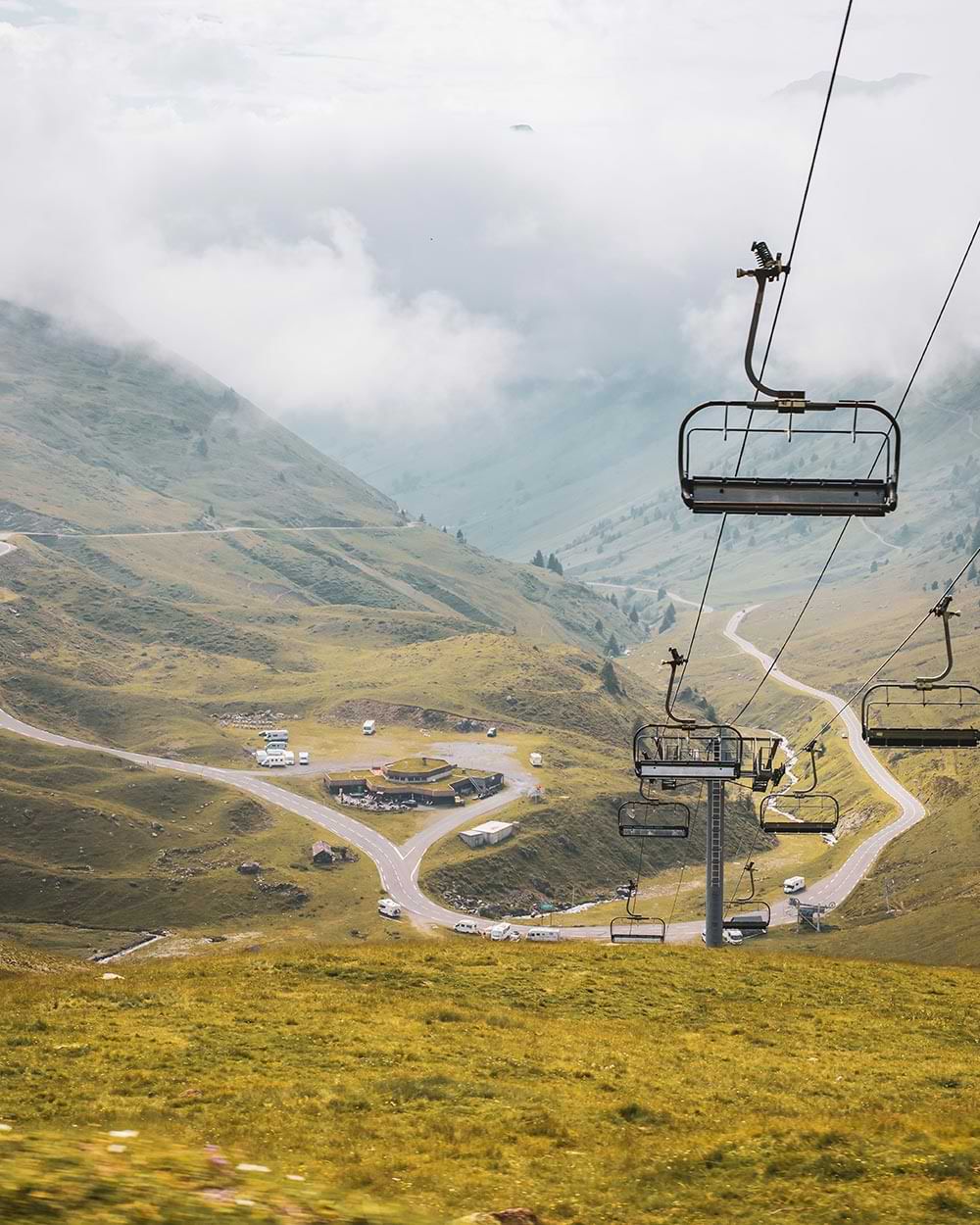 view from atop a hill of a chair lift travelling along the right and a low building resting toward the floor of a deep, and green valley