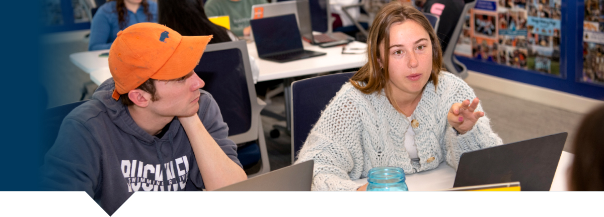 two students in computer lab having a conversation at a group table