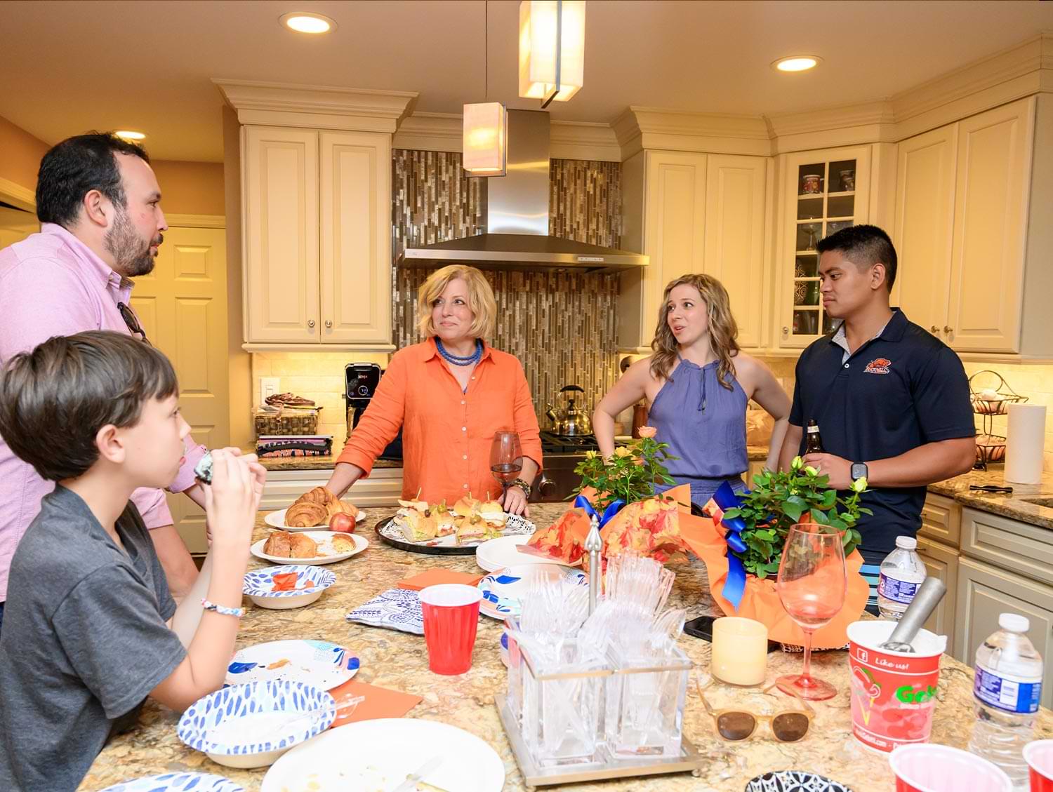 Peter Gale and son Preston with Susan Agostini, Danielle Agostini Gorospe and her husband, King Gorospe stand together in a home kitchen mingling over food