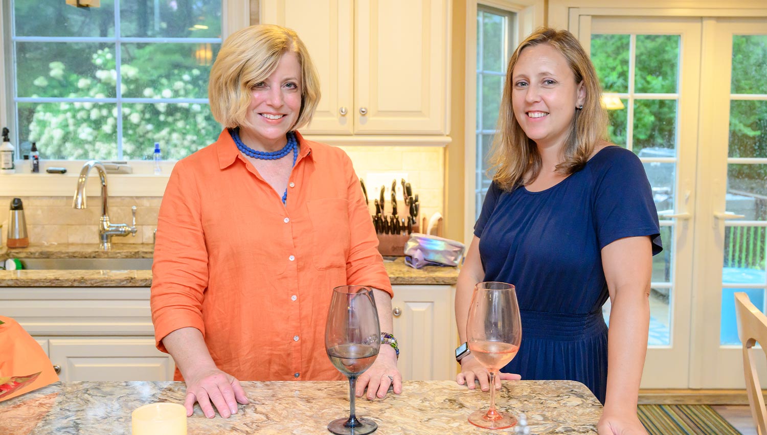 Susan Agostini and Caroline Robbins Gale stand beside each other smiling while standing in the kitchen at the Agostini home