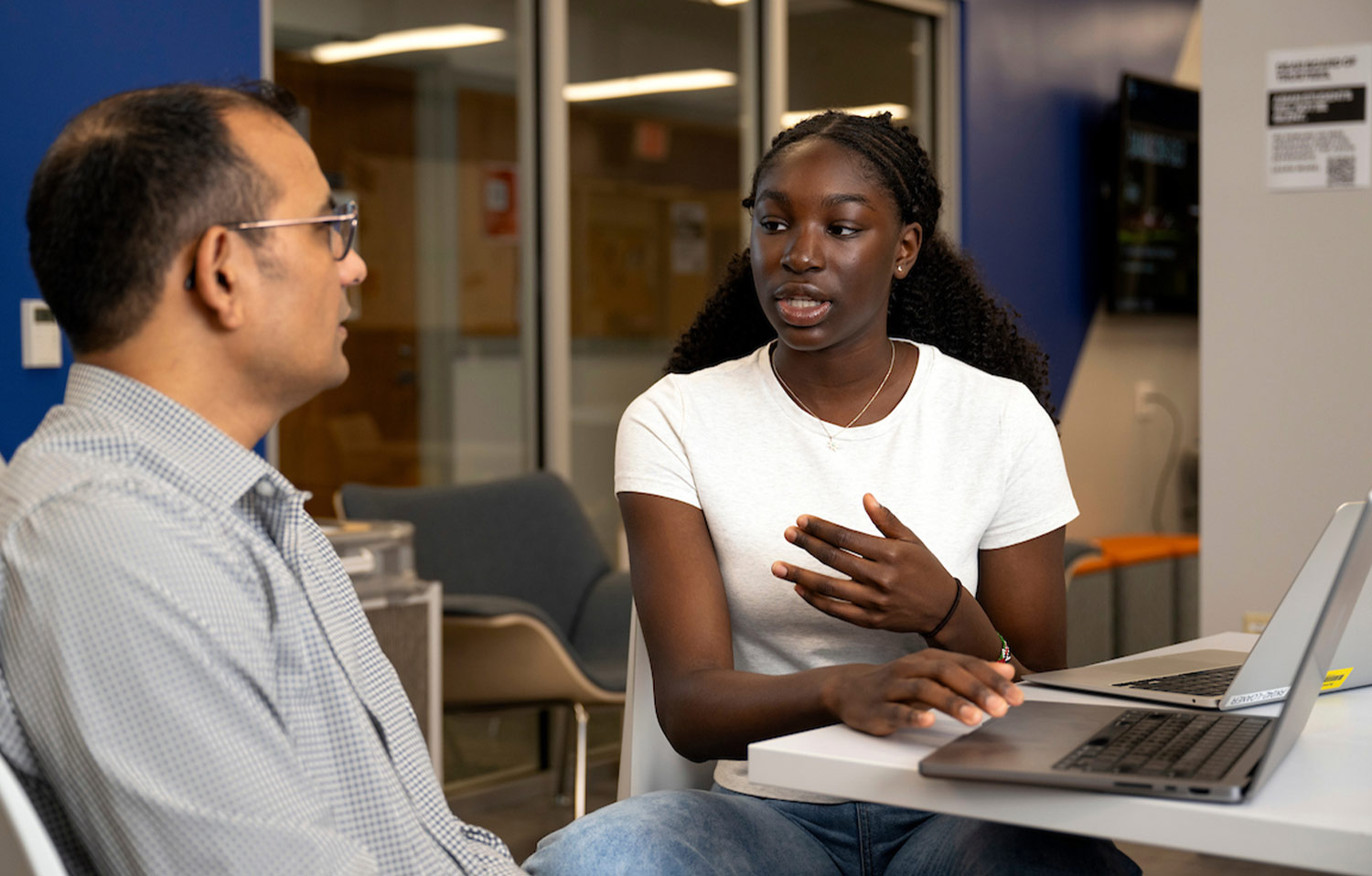 Amanda Agambire sit at a laptop in a workspace while in mid discussion with mentor Professor Rajesh Kumar