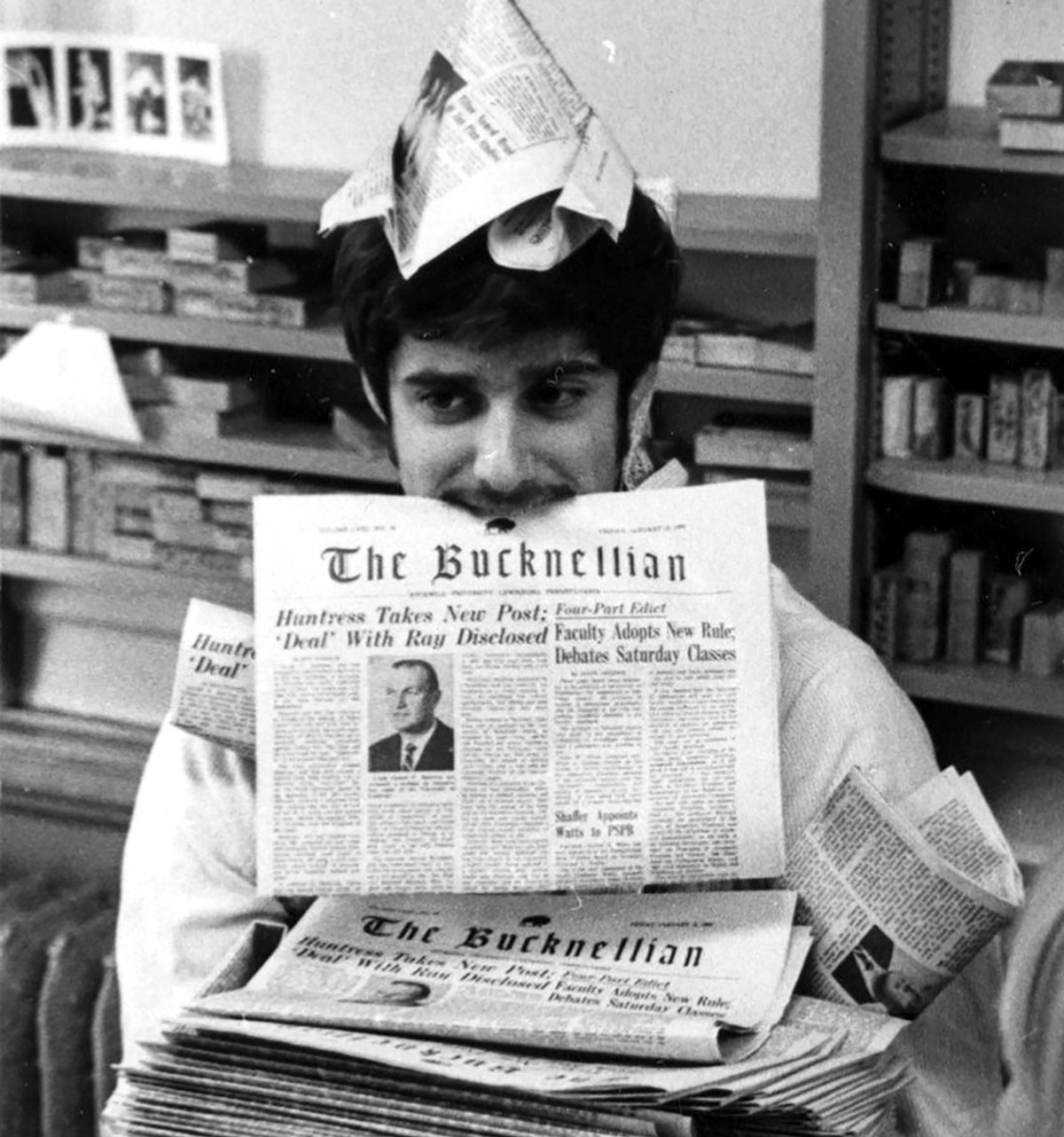 Vintage photo of a student under a stack of newspapers holding one between his teeth