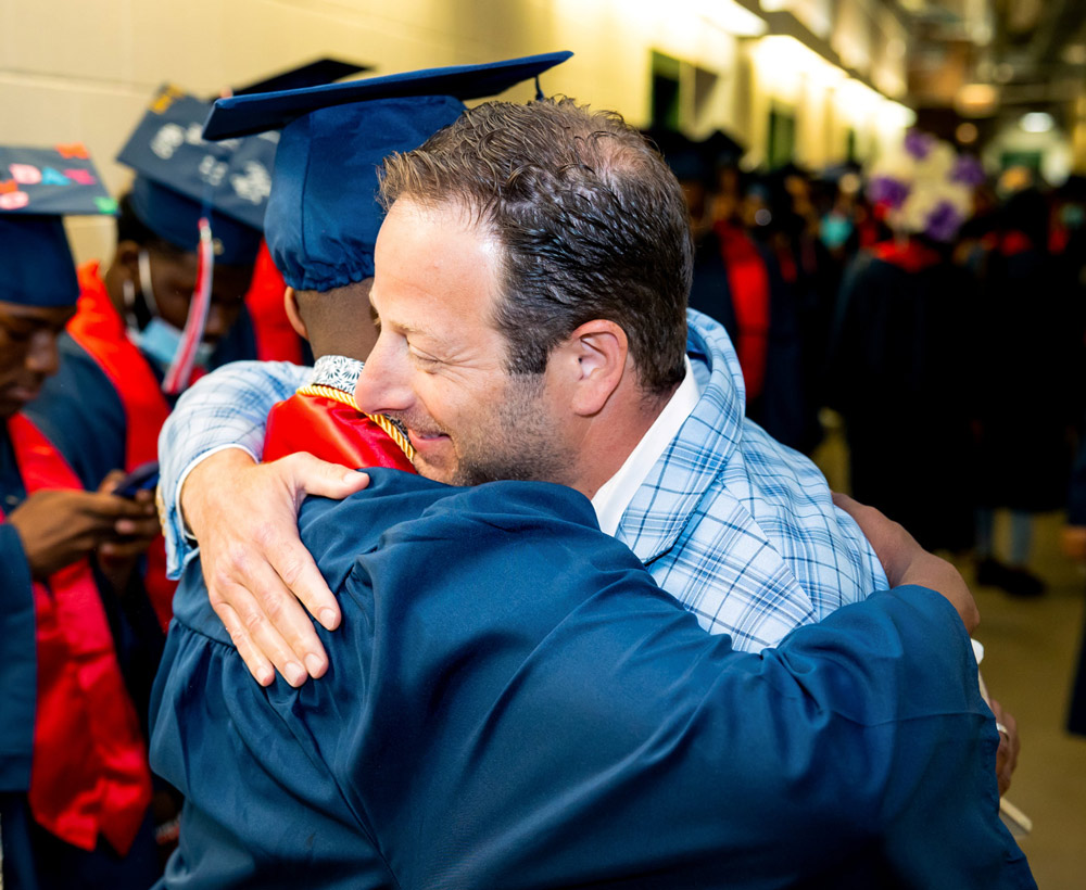 Pete Kadens hugging a student that's wearing a graduation cap and gown