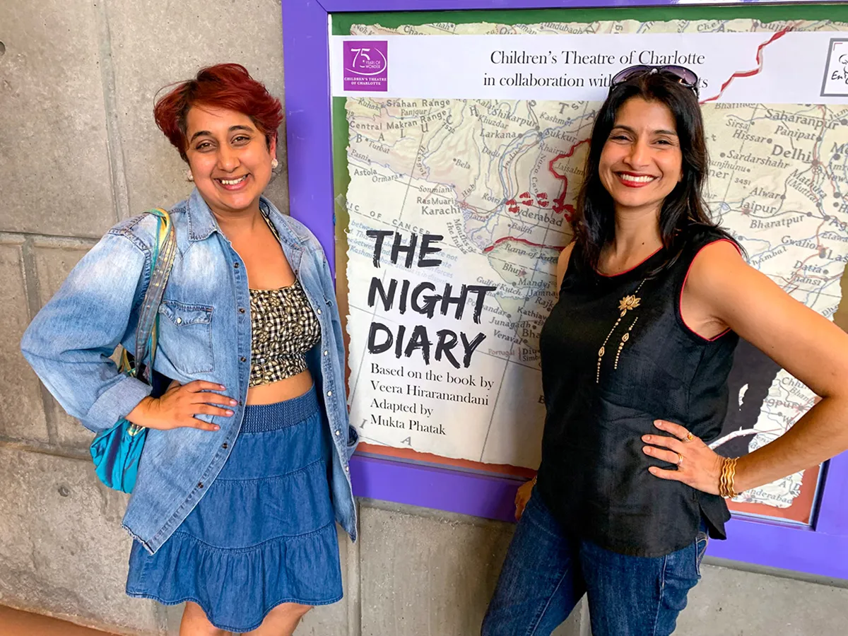 Mukta Phatak and Anjalee Deshpande Hutchinson pose together in front of their theatre poster