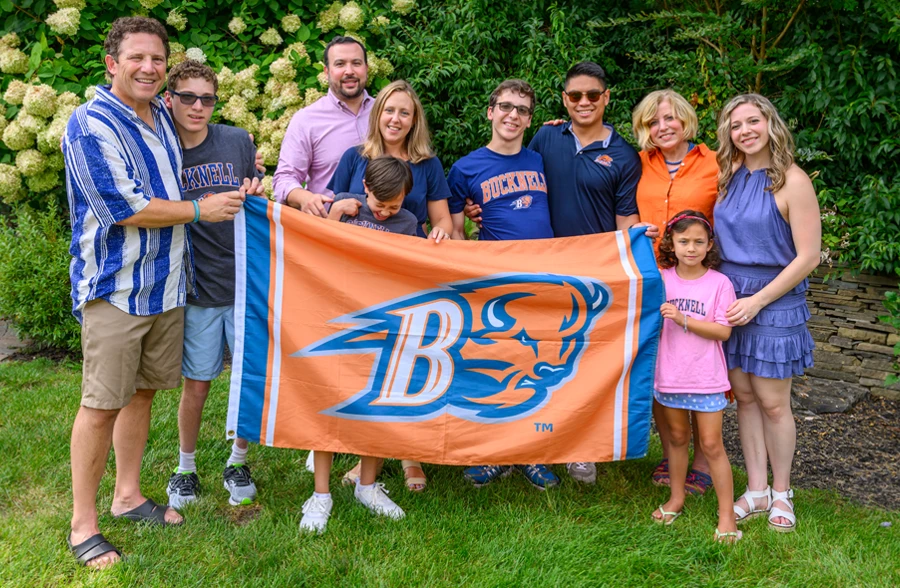 Peter and Susan Agostini and their children smiling on grass yard holding Bucknell orange and blue flag