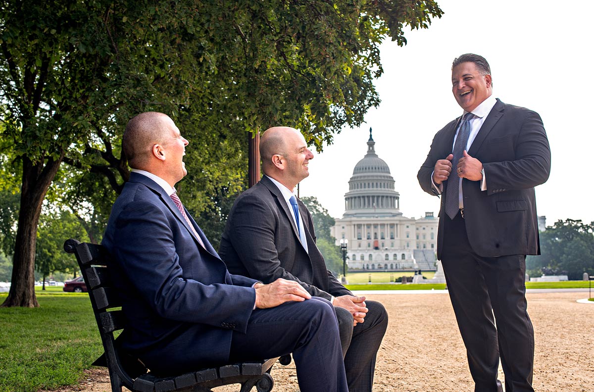 on a sunny day Darryl Volpicelli, Ed Currie, and Rob Canestrari have a laugh together while sitting on a bench on Capitol Hill