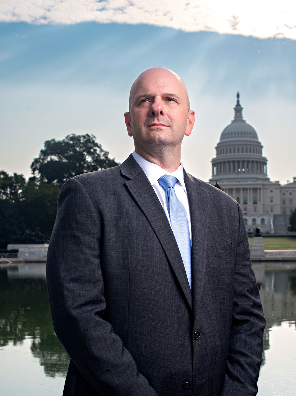 portrait of Darryl Volpicelli wearing a suit and standing against the Capitol building and its Reflecting Pool