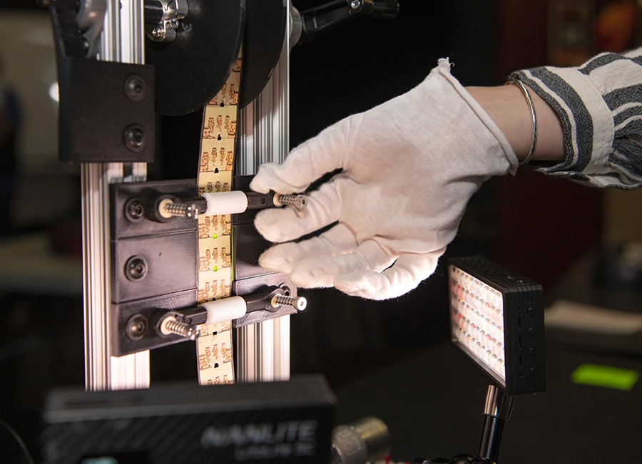 close up of a gloved hand working with film strips on a reel