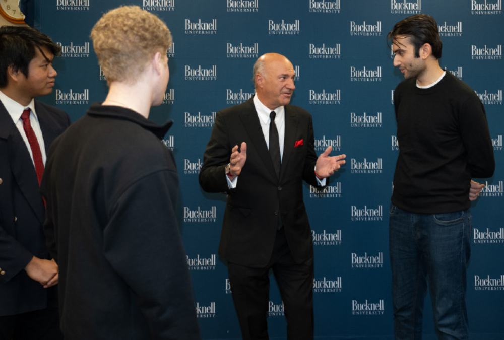 Forum speakers Jordy Leiser, Alex Rodriguez, Marc Lore, Kevin O’Leary and George Takei engaged in conversation in front of a backdrop with the words "Bucknell University" repeated across it.