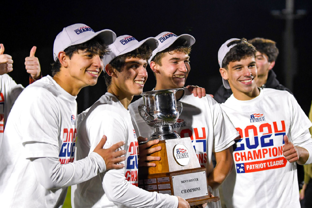 Group photo of soccer players smiling and holding trophy.