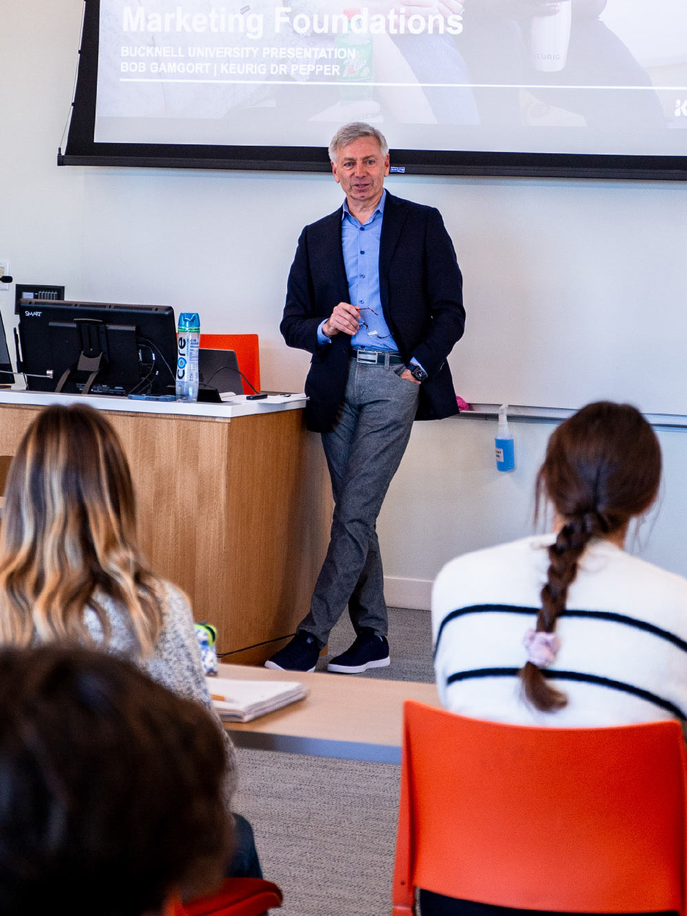 Bob Gamgort stands at the front of a lecture hall, addressing a group of people who are seated facing him.