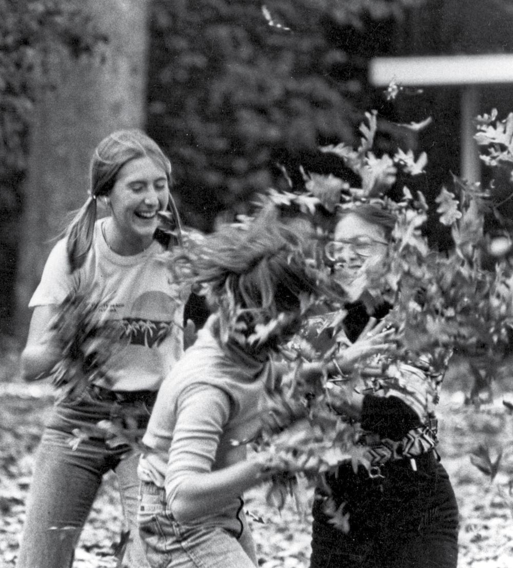 Three young people playing and throwing leaves in an outdoor autumn setting.