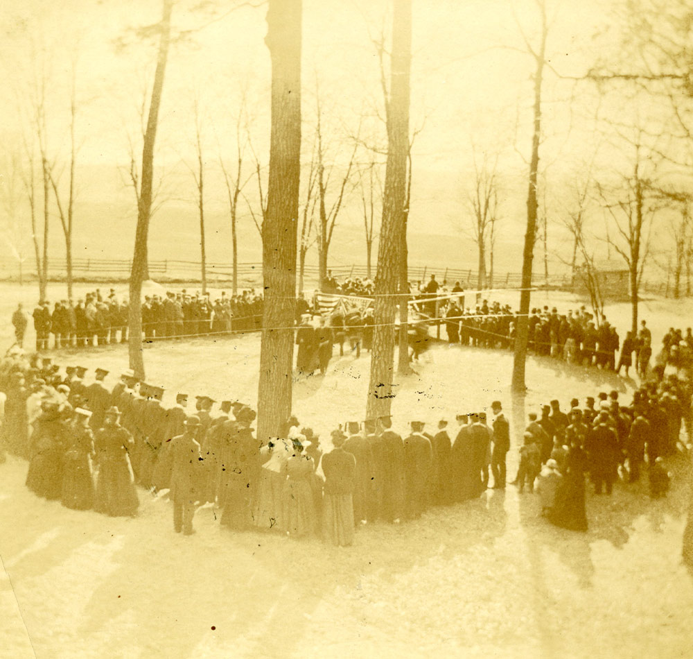 high angle faded image of a large event gathering held in a wooded grassy area