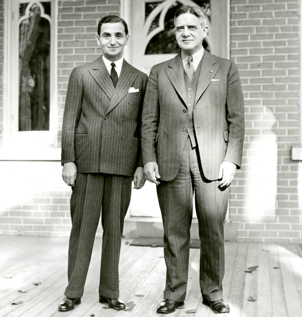 black and white image of Irving Berlin H’40 (top, left) with another man, both stand on the porch of a brick building