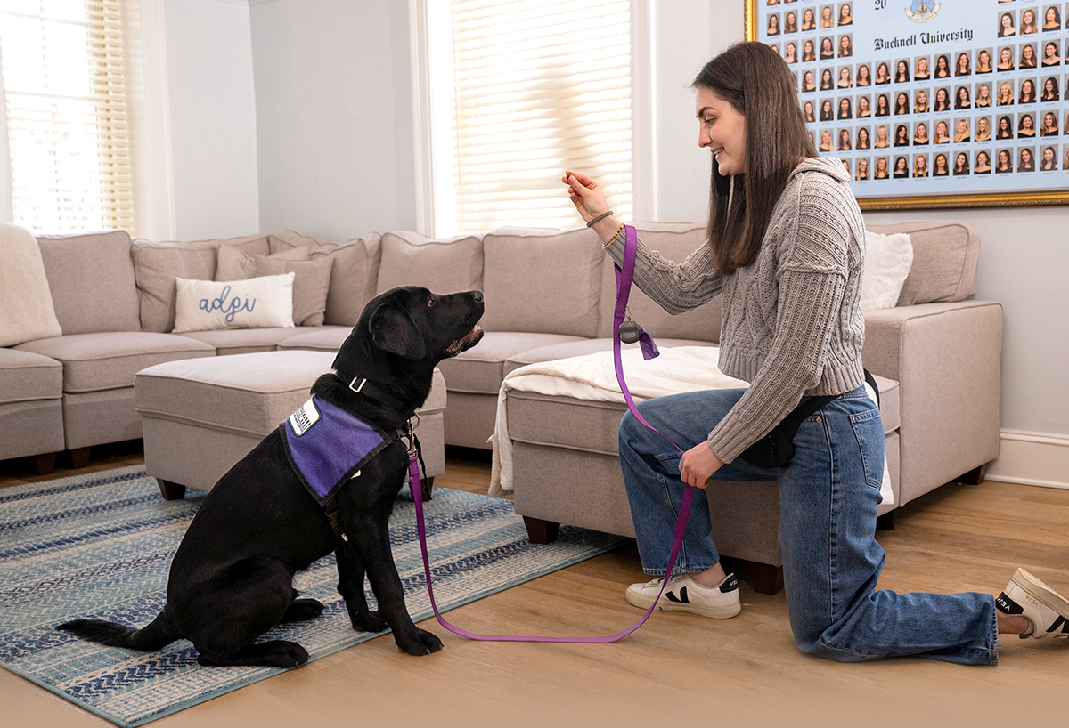 Emma Feld on one knee giving her dog a treat while it's sitting