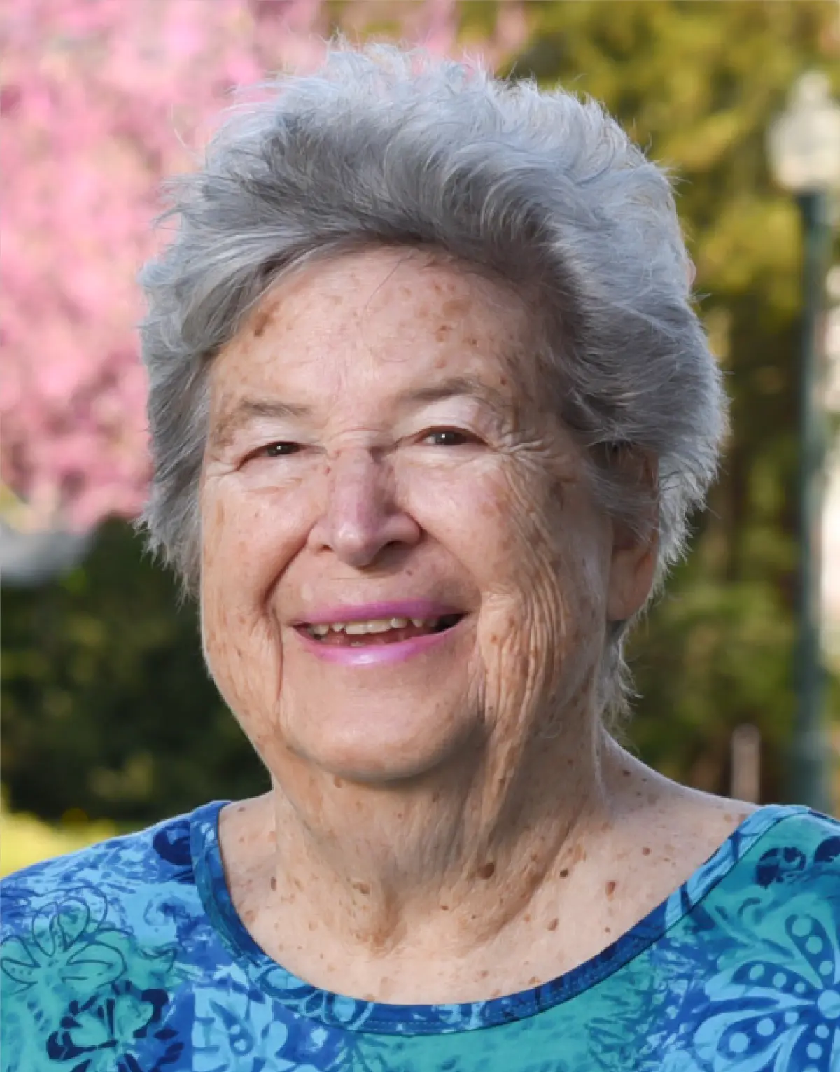 Portrait orientation outdoor photograph headshot view of Josephine Hildreth Detmer smiling in a multi-colored floral pattern style t-shirt (turquoise/dark blue/light blue)